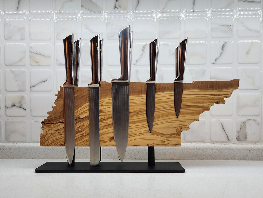 Set of knives on a wooden stand shaped like the state of Tennessee against a marble wall.