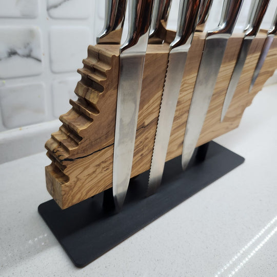 Set of knives with wooden handles in a black stand on a kitchen counter.