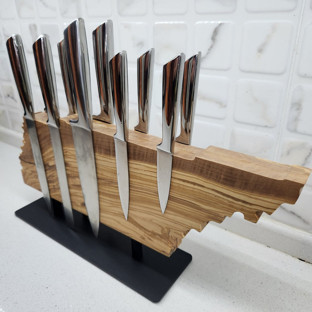 Set of knives in a wooden block on a stand against a marble wall.