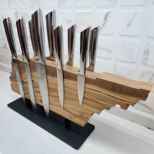 Set of knives in a wooden block on a stand against a marble wall.